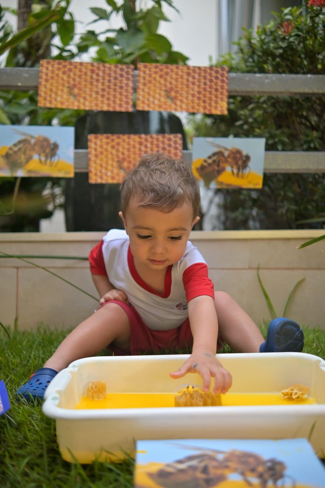 Criança explorando com as mãos uma bacia de objetos, diante de um painel de texturas