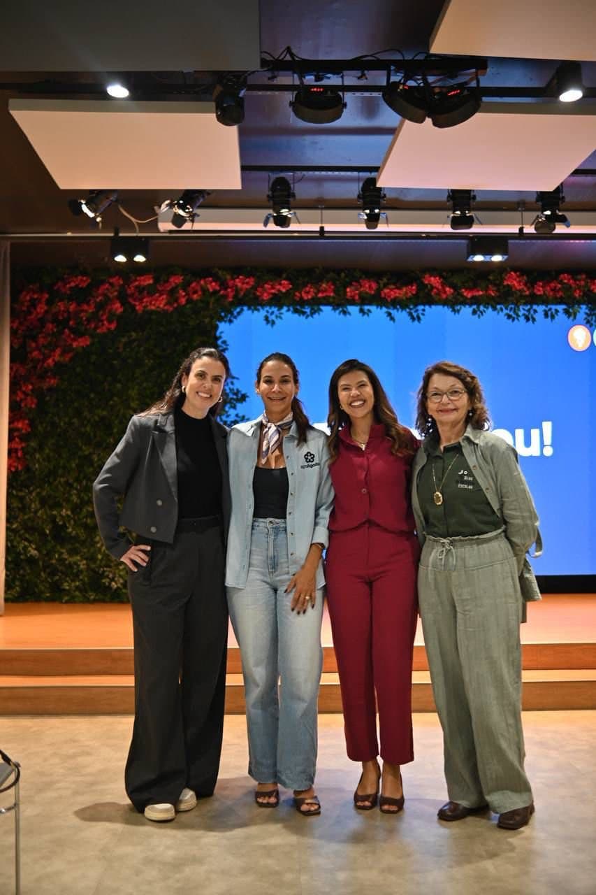 Quatro mulheres lado a lado no palco do auditório, diante do telão
