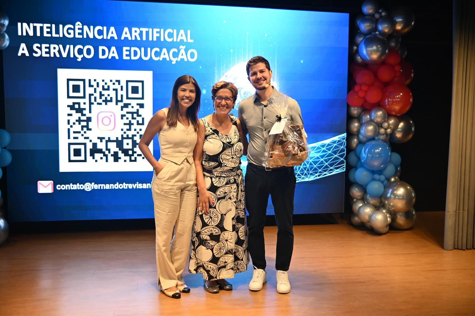 Duas educadoras e o palestrante no palco, diante do telão da palestra sobre inteligência artificial na educação